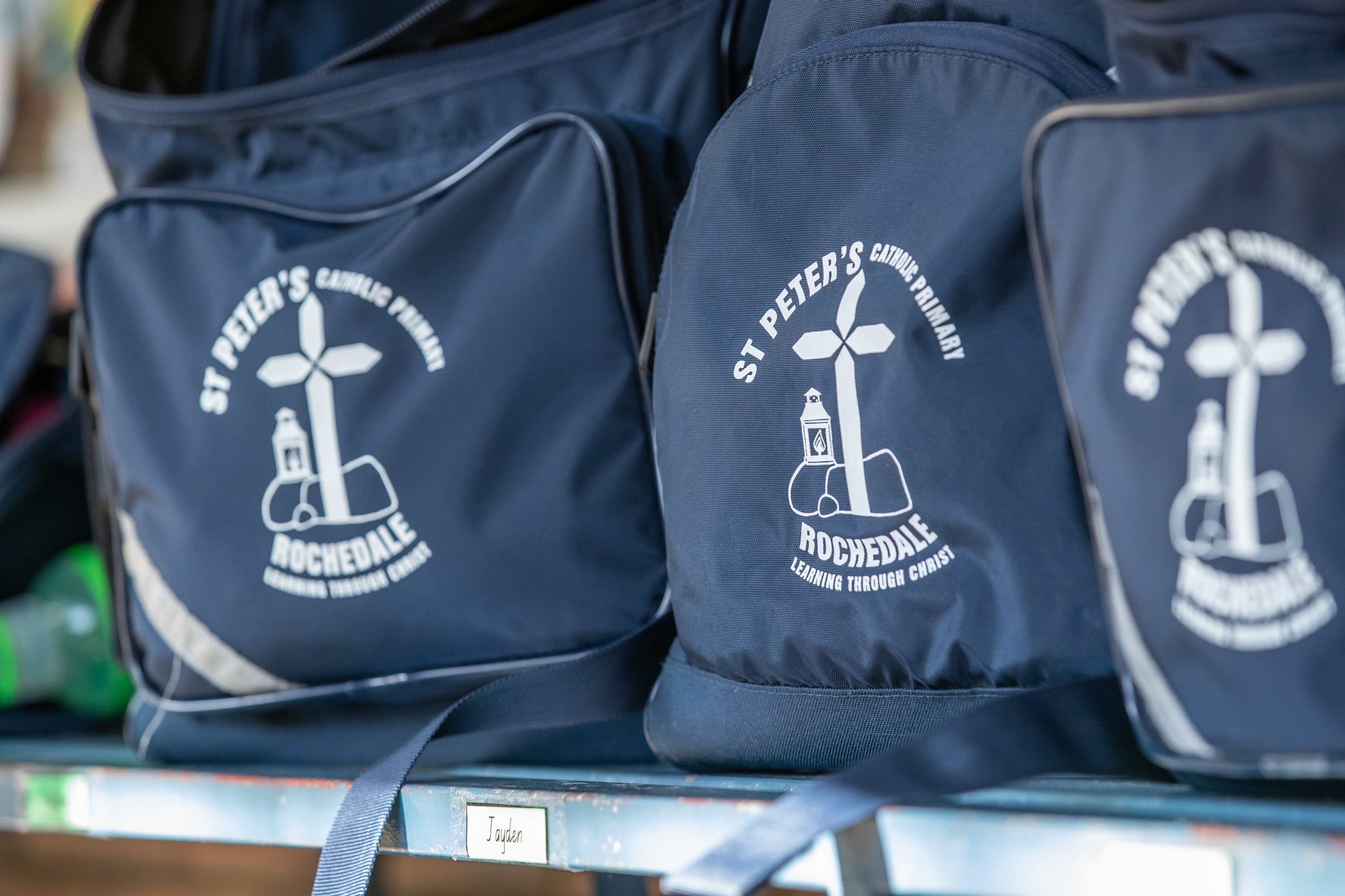 School bags with St Peter’s Catholic Primary Rochdale logo displayed on a shelf representing school identity