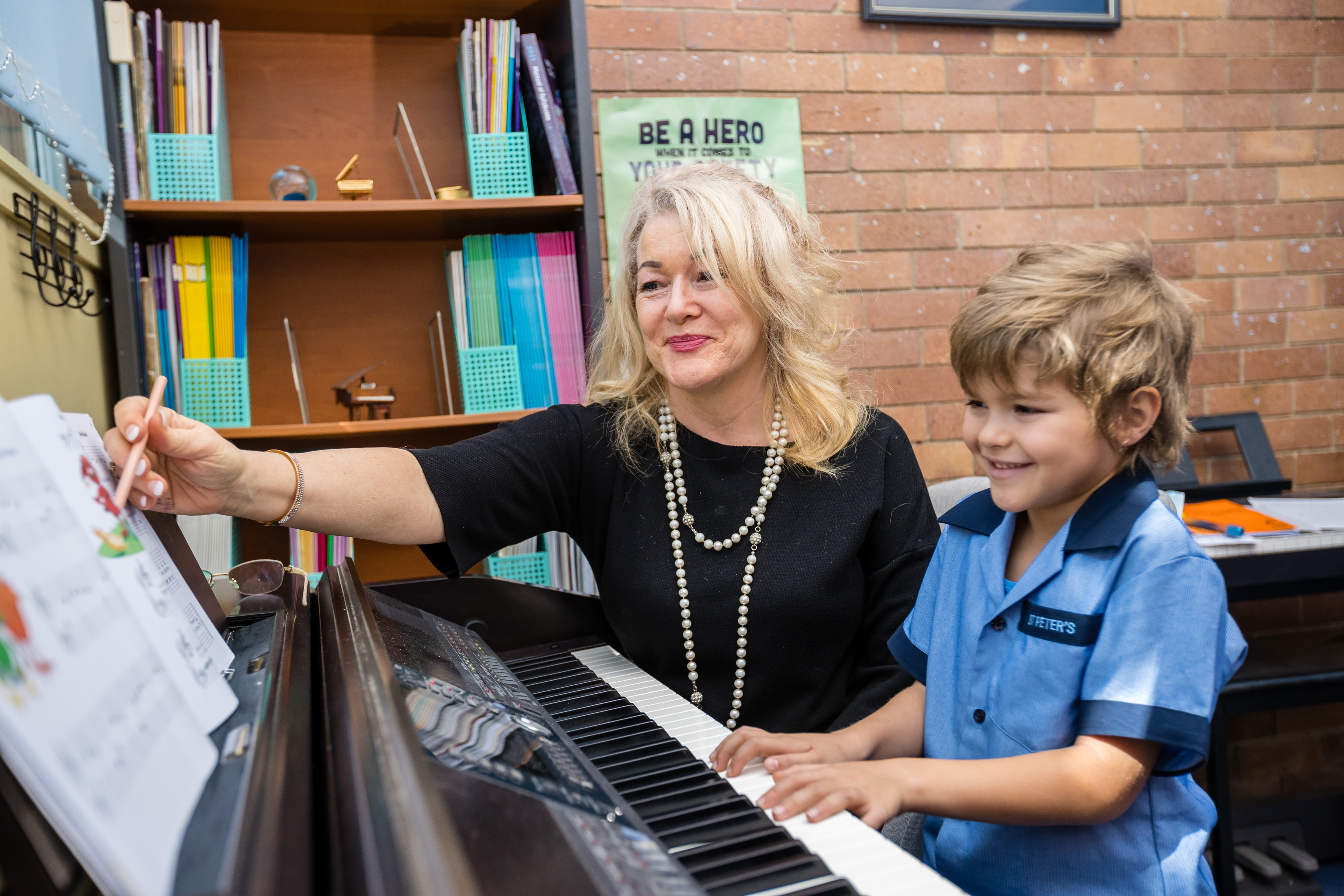 Teacher supporting a student during a piano lesson with sheet music while building music skills in a classroom setting