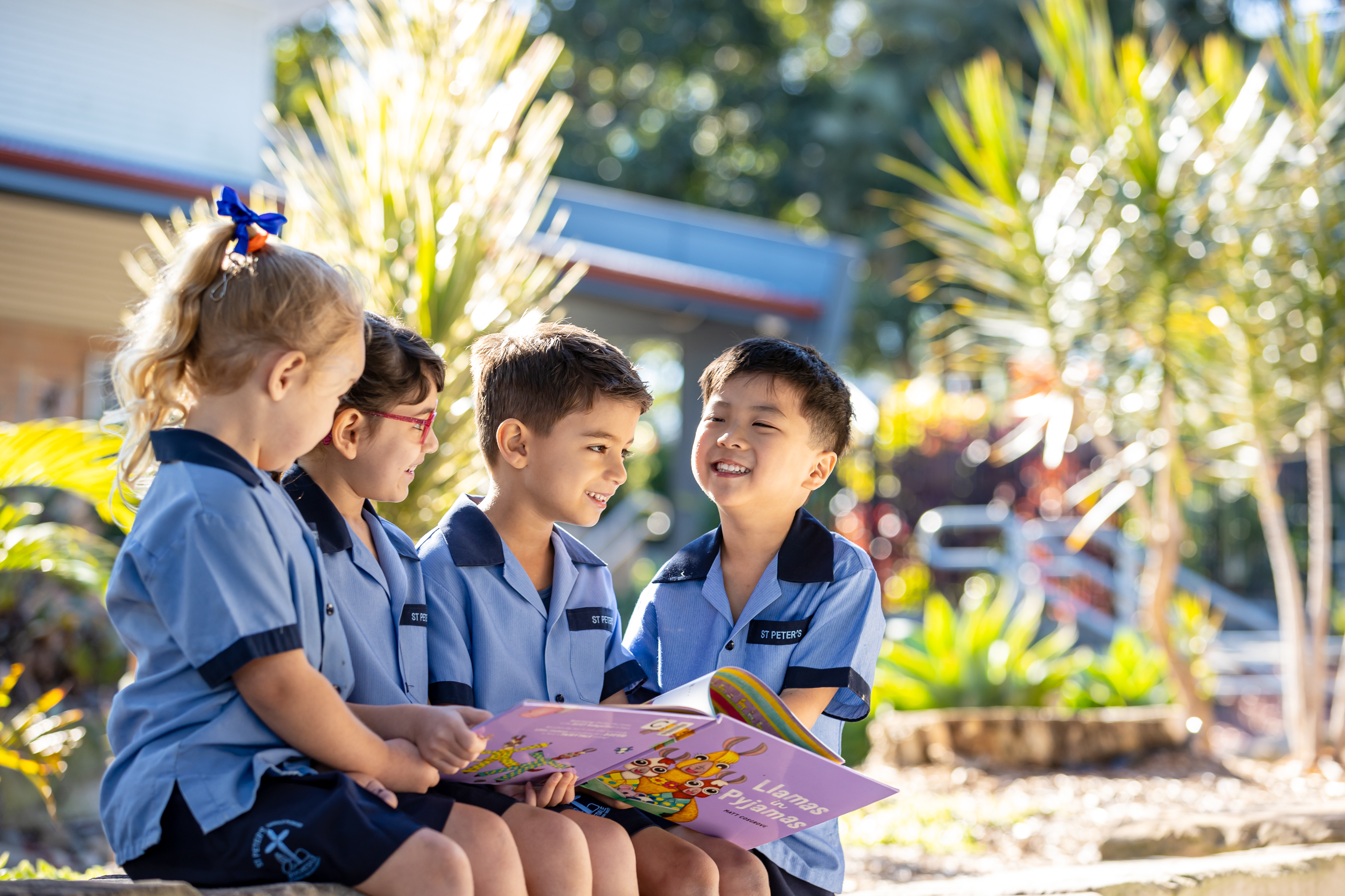 Students sitting outdoors reading a book together in a school setting, sharing learning and conversation