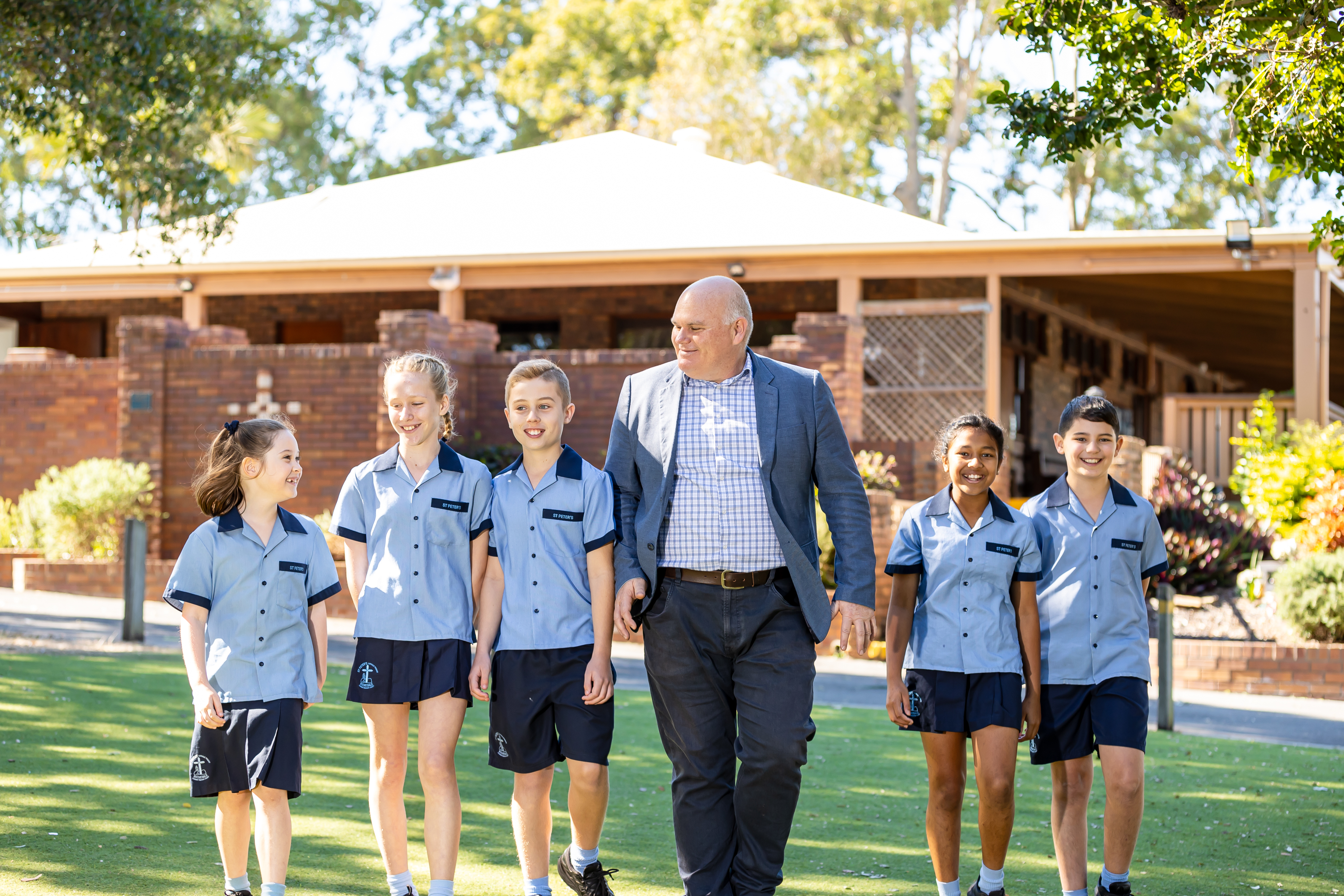 Principal Michael McInerney walking with students in school uniform across the campus grounds, engaging with the school community