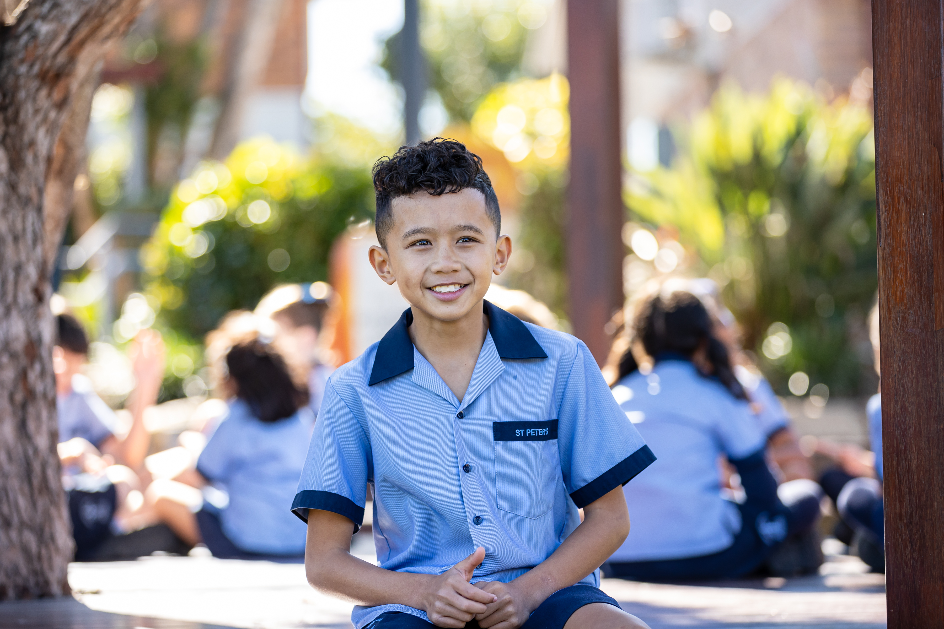Student in school uniform smiling outdoors on campus with other students gathered in the background