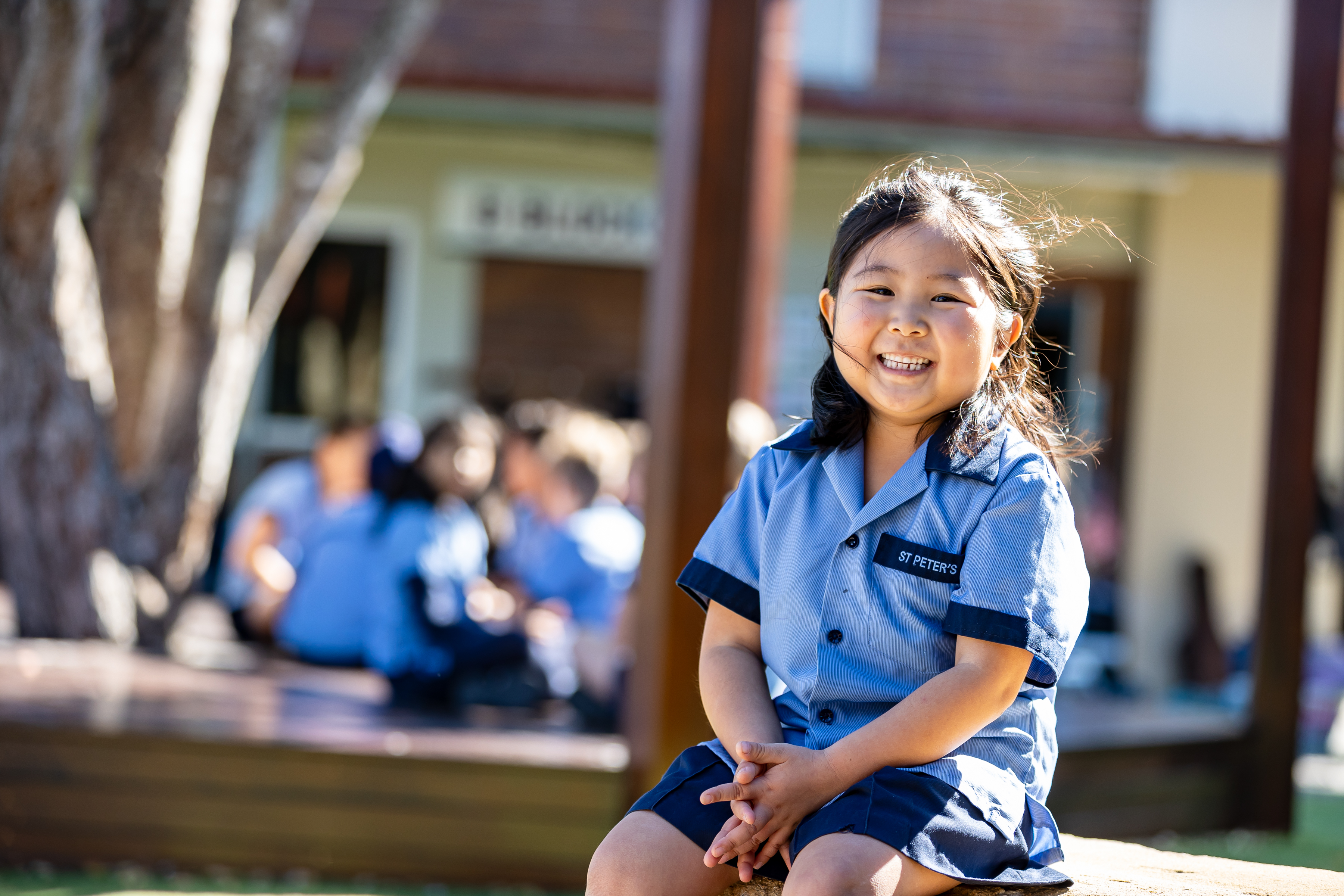 Student in school uniform sitting outdoors on campus with other students gathered in the background